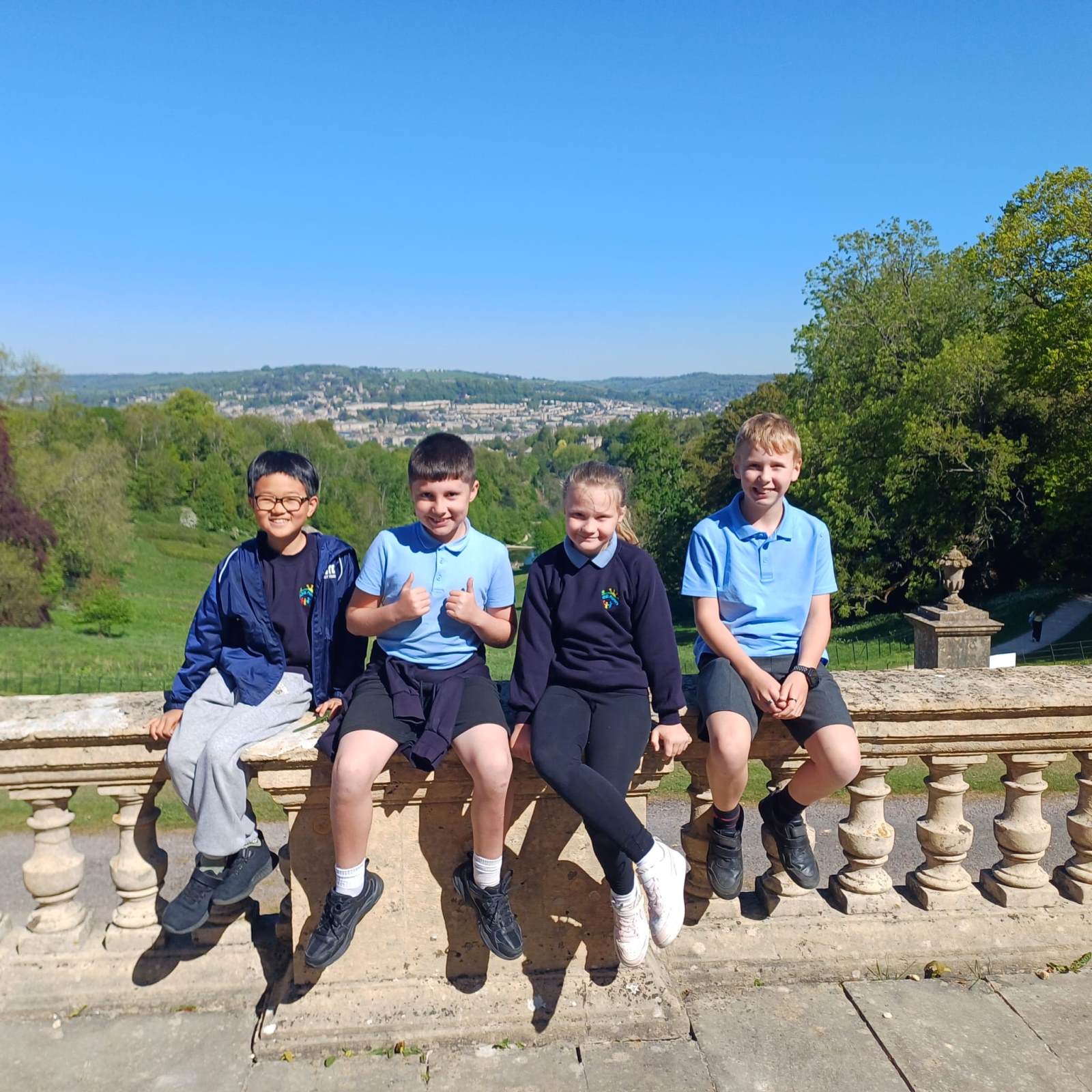 four children sitting on a stone wall with the background of Prior Park Landscape Garden in Bath